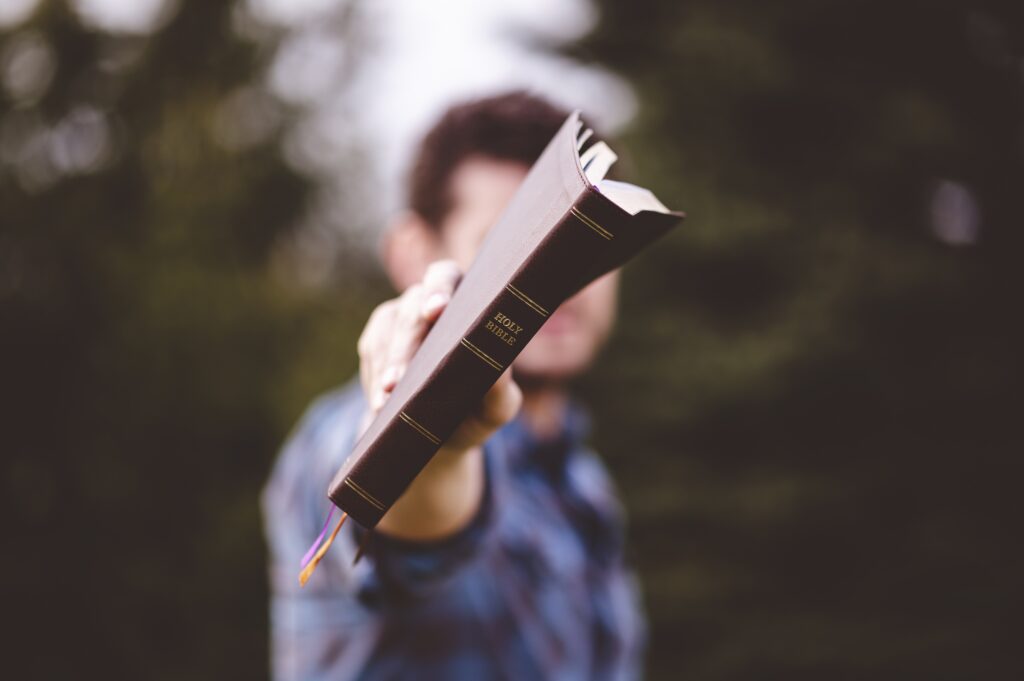 selective focus shot of a male standing and holding a book in hands